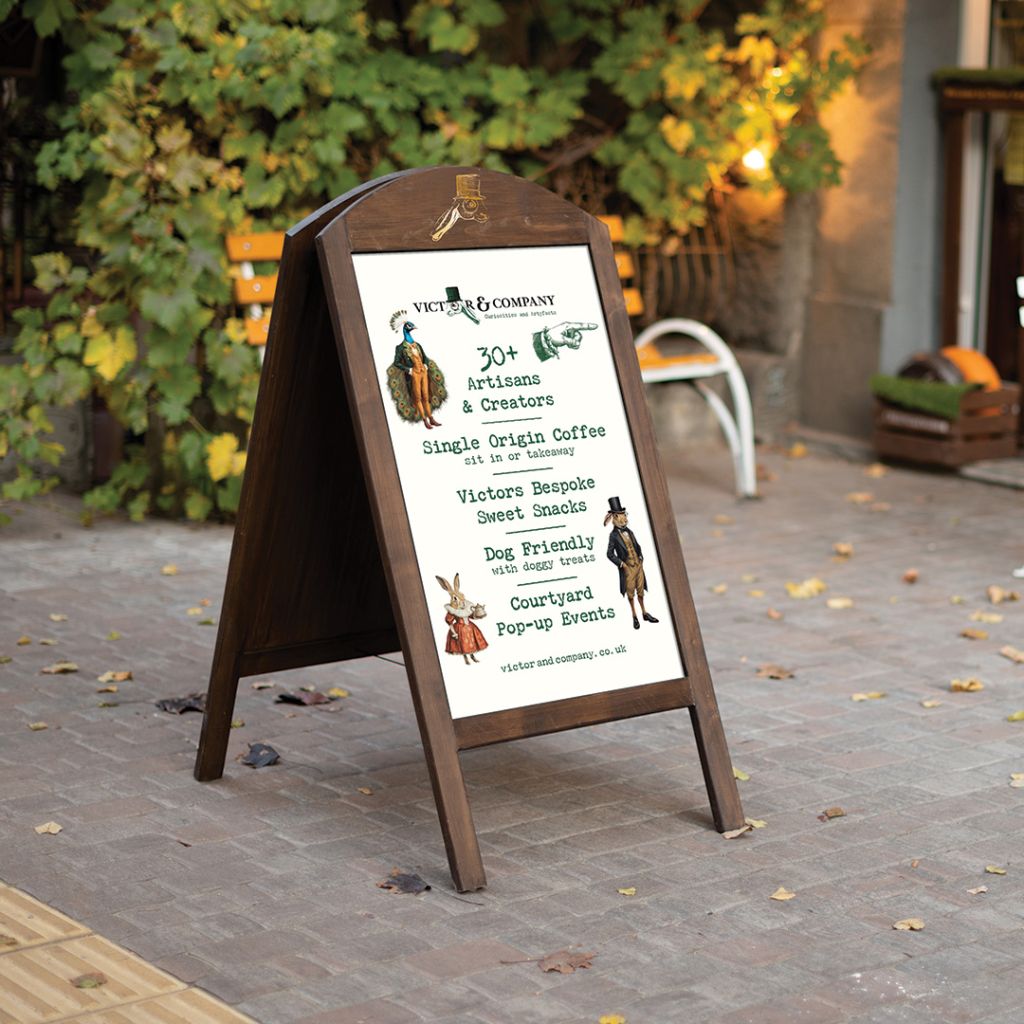 Traditional wooden A-board pavement sign with custom-designed inserts promoting "30+ Artisans," coffee, and dog-friendly events in Long Melford.